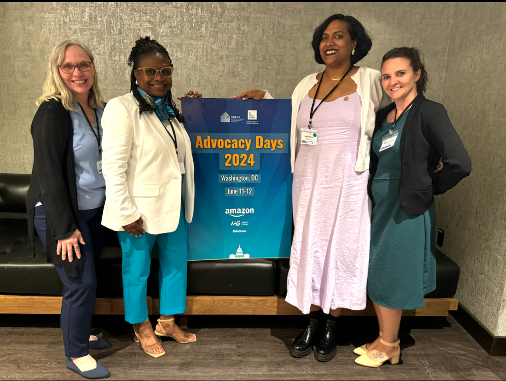 Two white women and two Black women stand around a sign titled with the words "Advocacy Days 2024 in Washington DC, June 11-12.